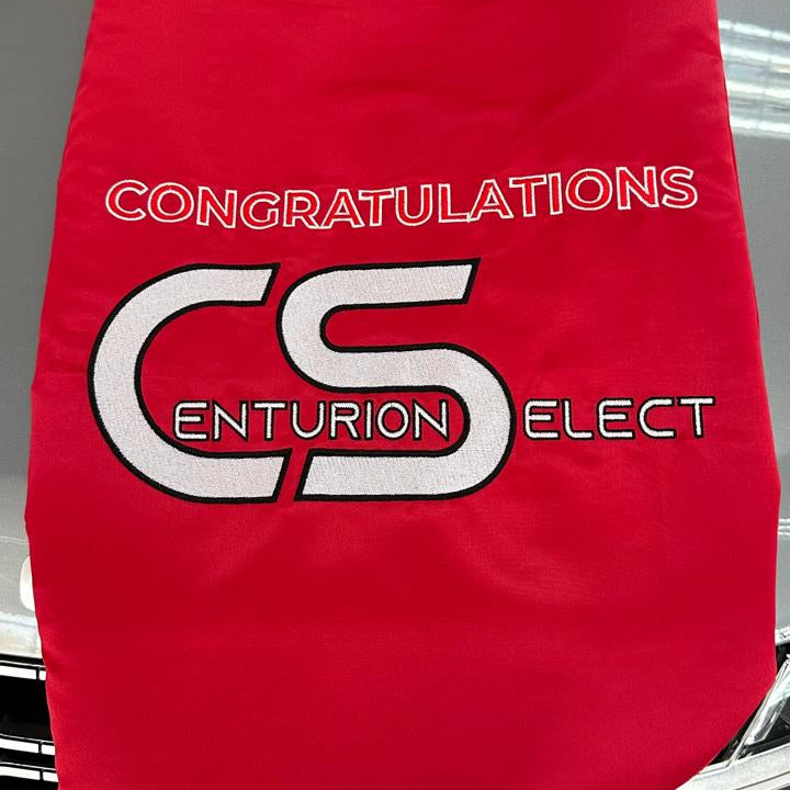 Red bow with 'Congratulations Centurion Select' text draped over a car grille.