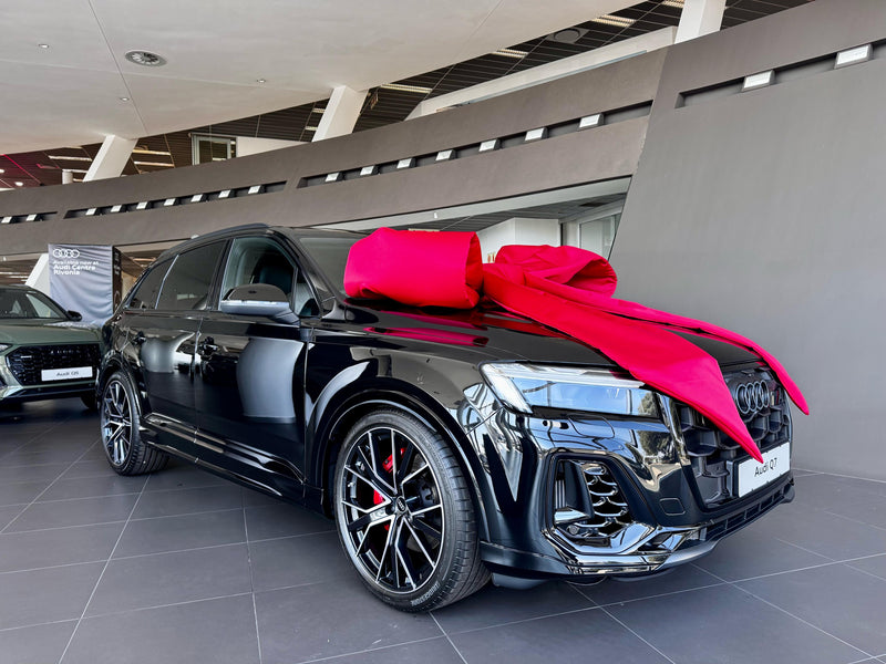 Black Audi SUV with an extra large red bow in a showroom setting